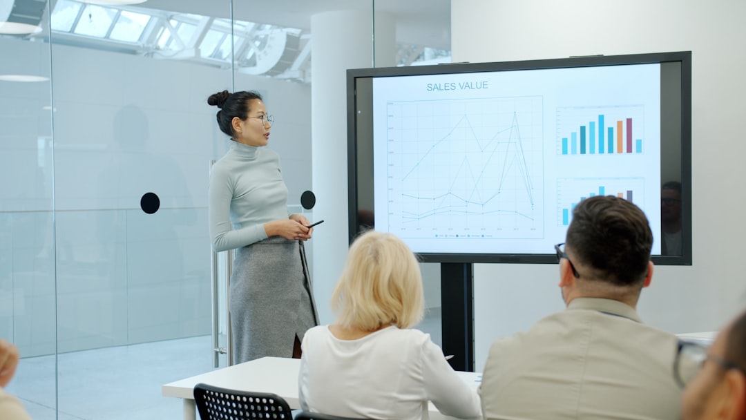 Cheerful Asian girl in formal clothing is speaking about marketing research in conference room while diverse group of people is listening and learning.