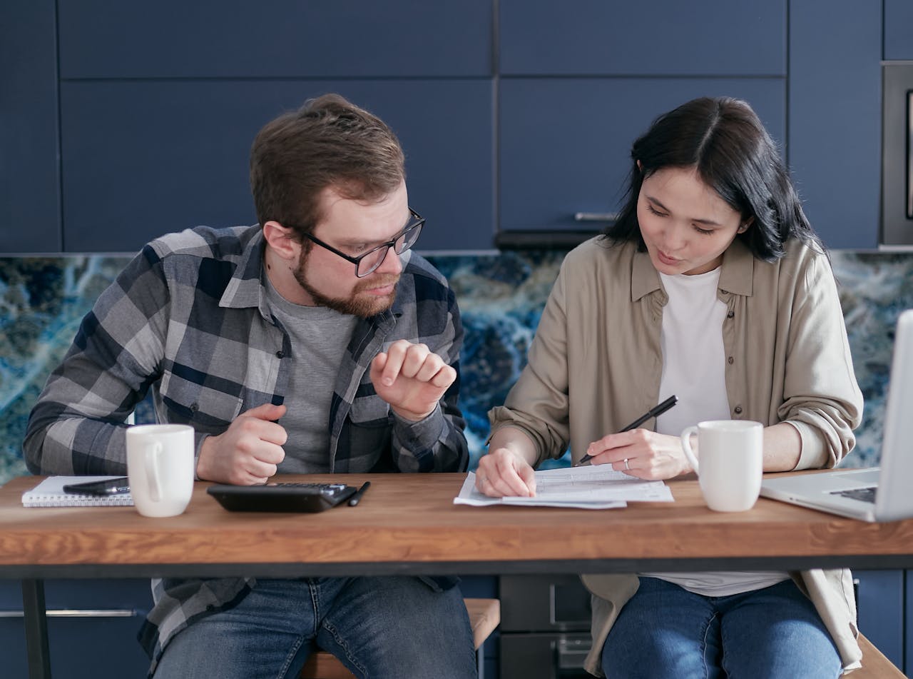 A couple sitting at a wooden table reviewing documents and discussing finances.